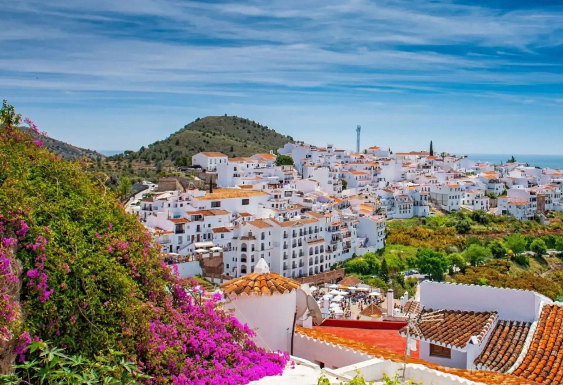 Charming whitewashed village nestled in green hills with vibrant flowers in the foreground.