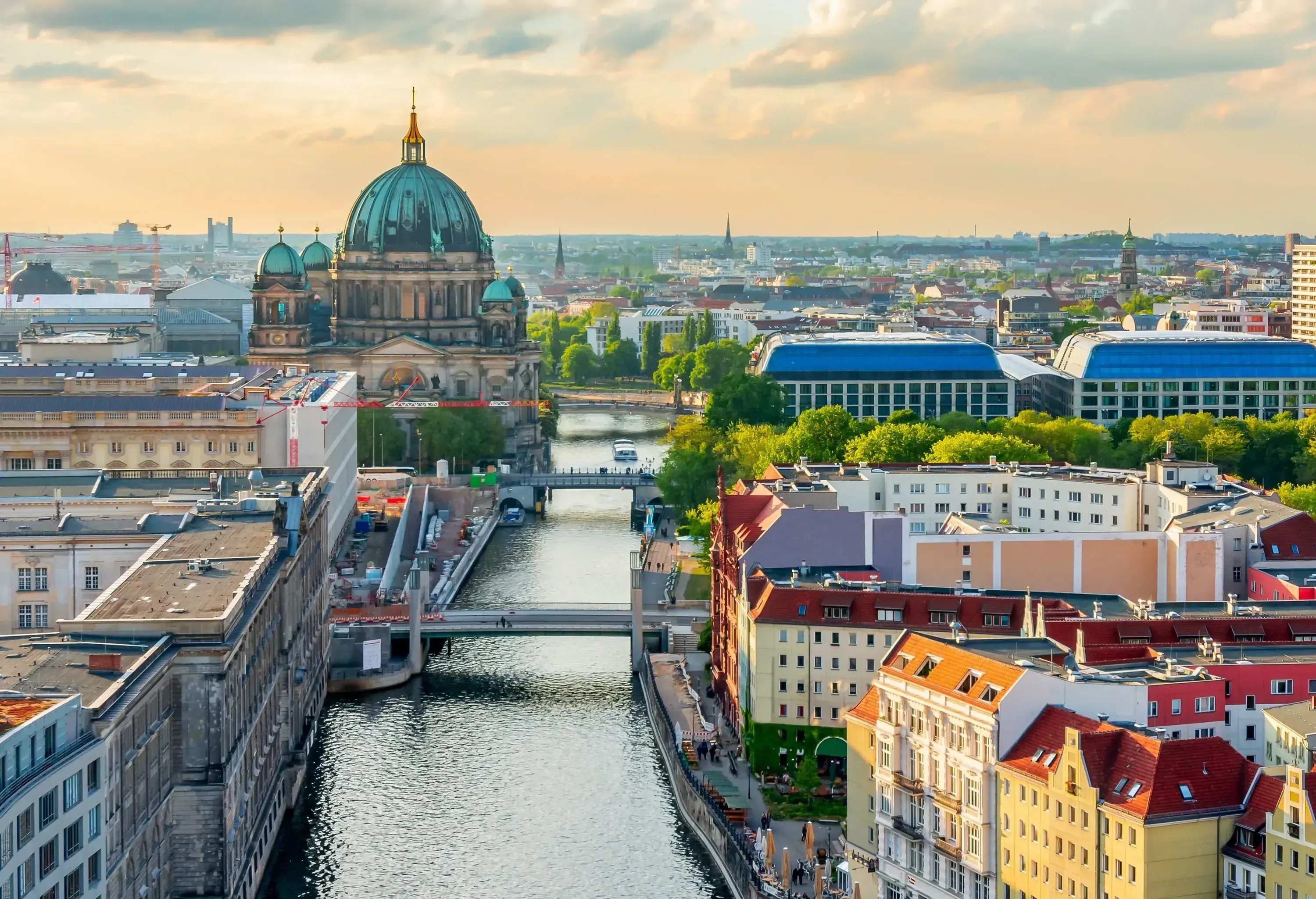 Aerial view of a cityscape with a wide river, a prominent domed structure, and numerous bridges and buildings at sunset.