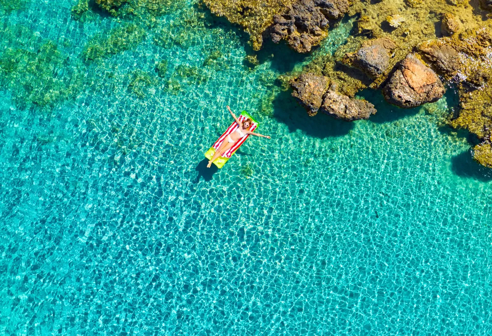 Person floating on raft in clear turquoise water near rocky shore