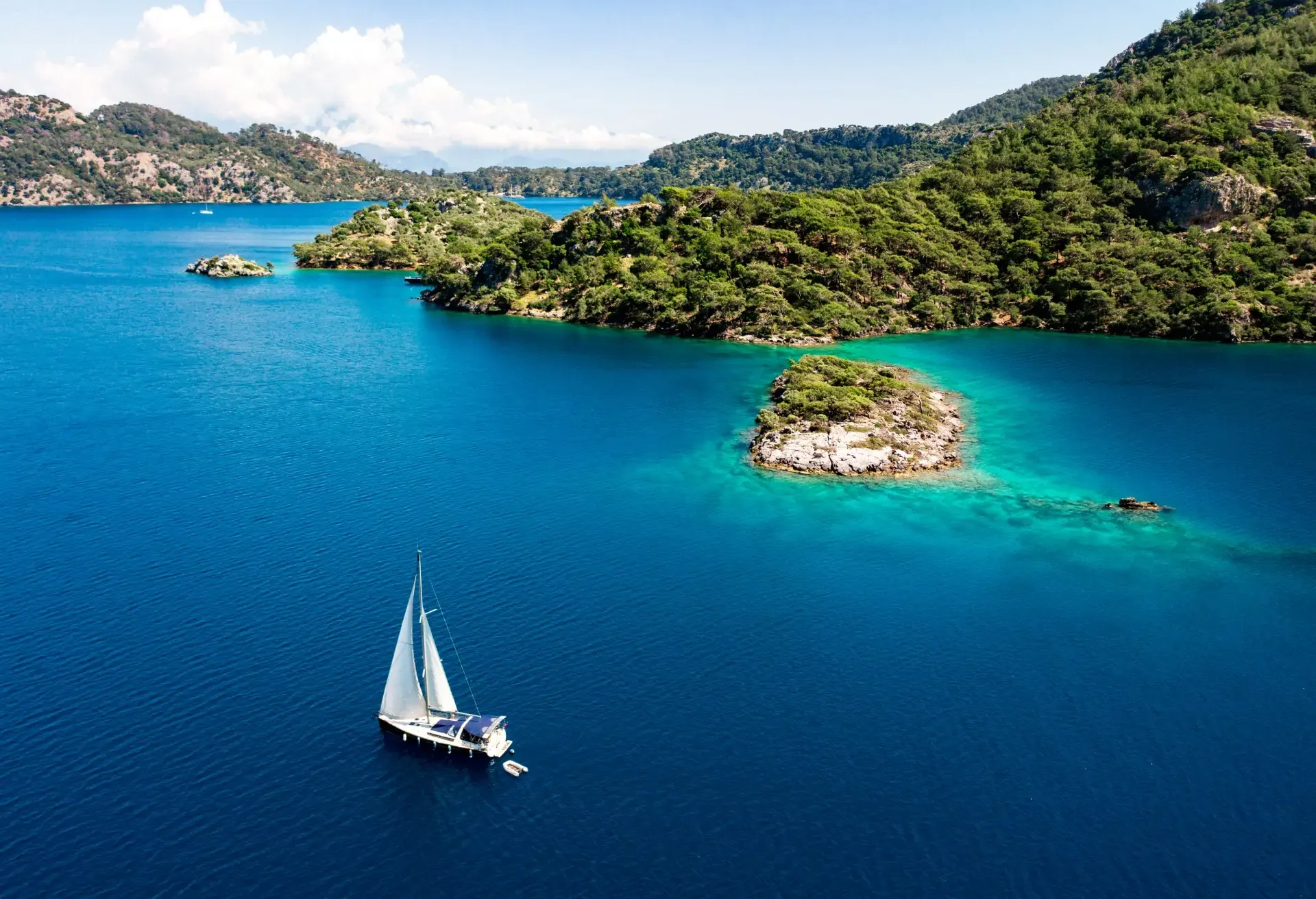 Sailboat on turquoise sea near lush green islands under clear sky