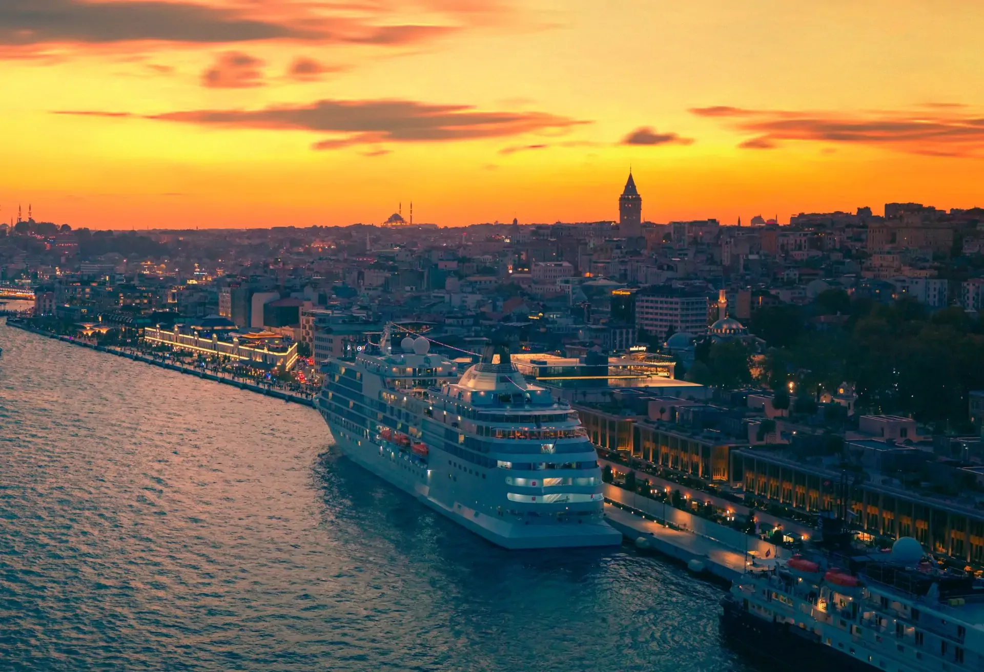Cruise ship docked along city waterfront at sunset with skyline silhouette